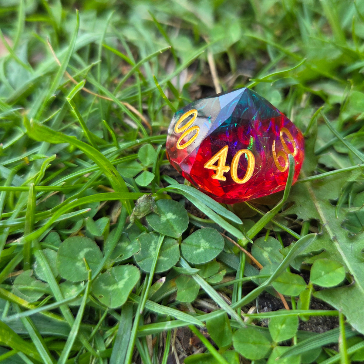 Blue and red percentile die seated on a bed of grass and clover