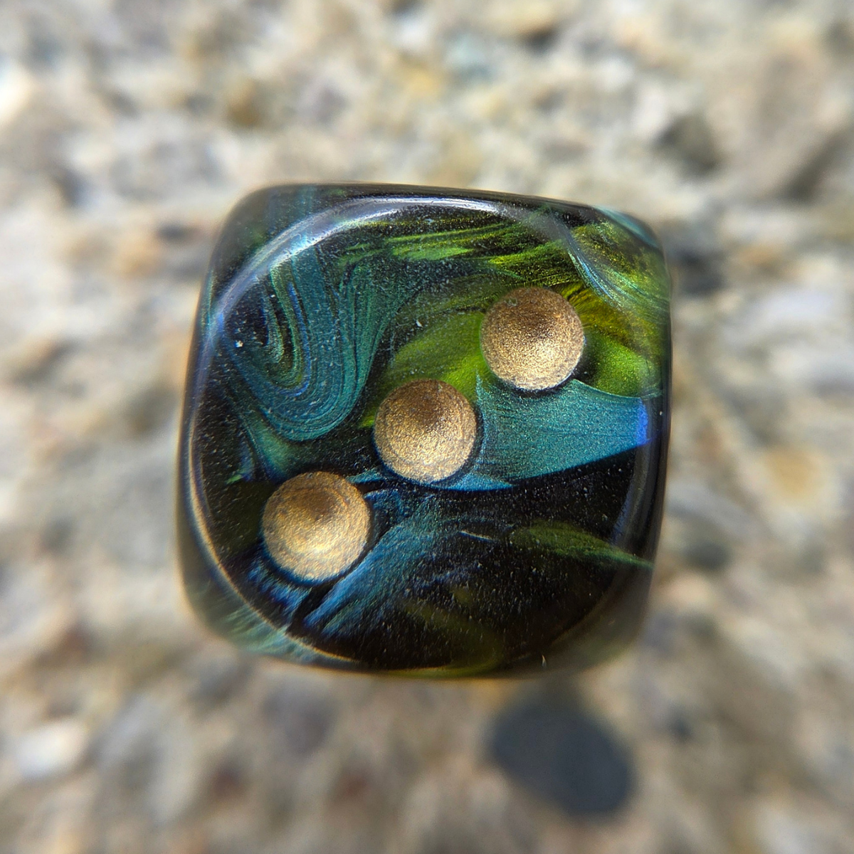 marbled green die with golden pips sitting on a textured rock