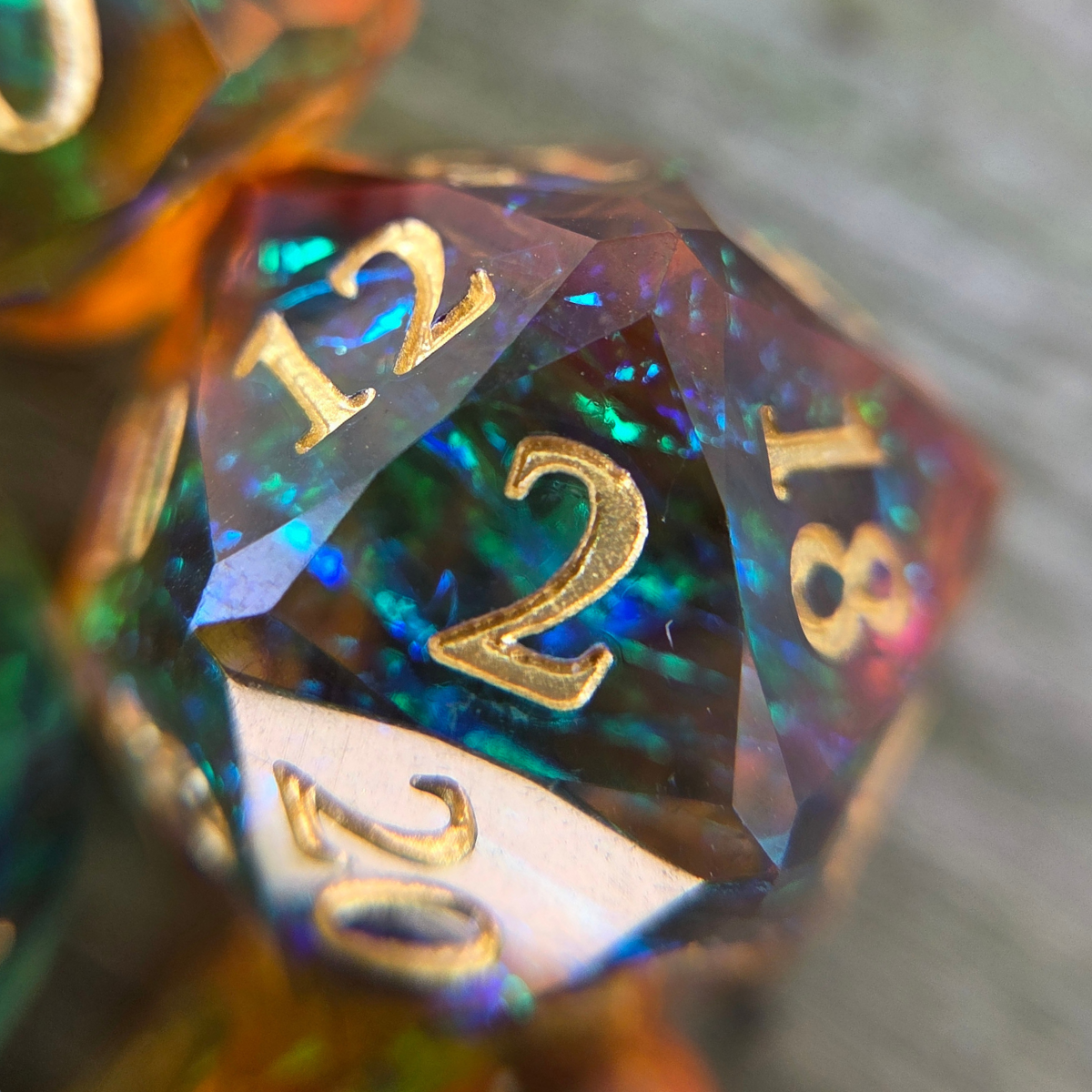 Close up of the 2 face of a d20 containing holographic foils, gold numbers, and a unique gem-like shape