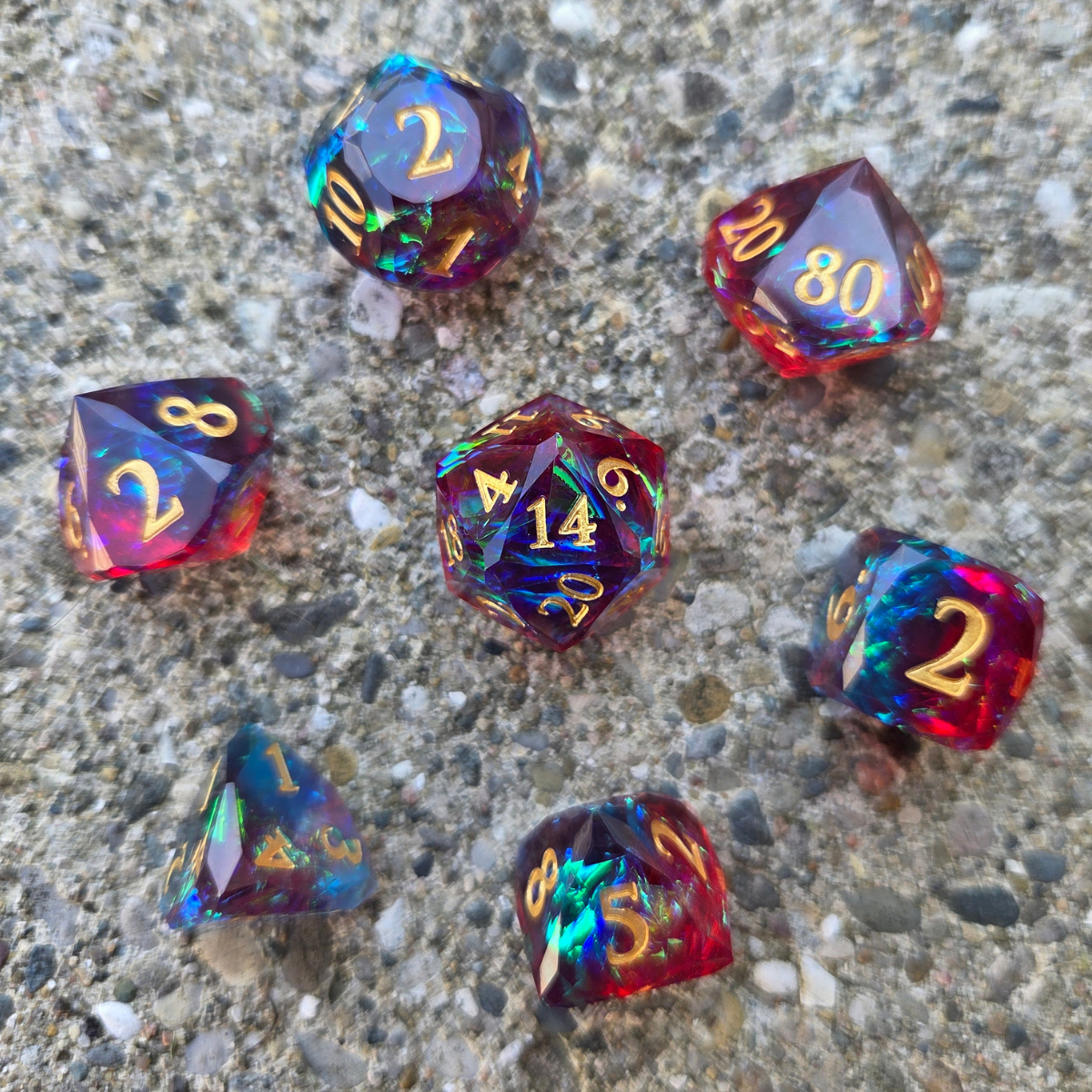Set of colorful polyhedral dice with gold numbers, sitting on a concrete surface