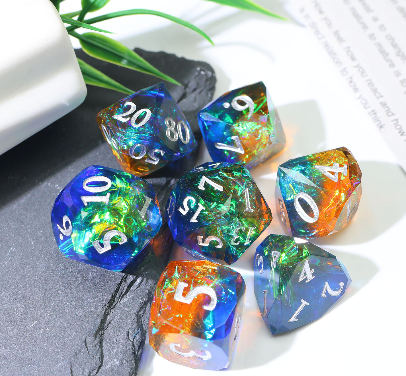 a set of colorful and faceted gaming dice sitting half on a stone and half on paper