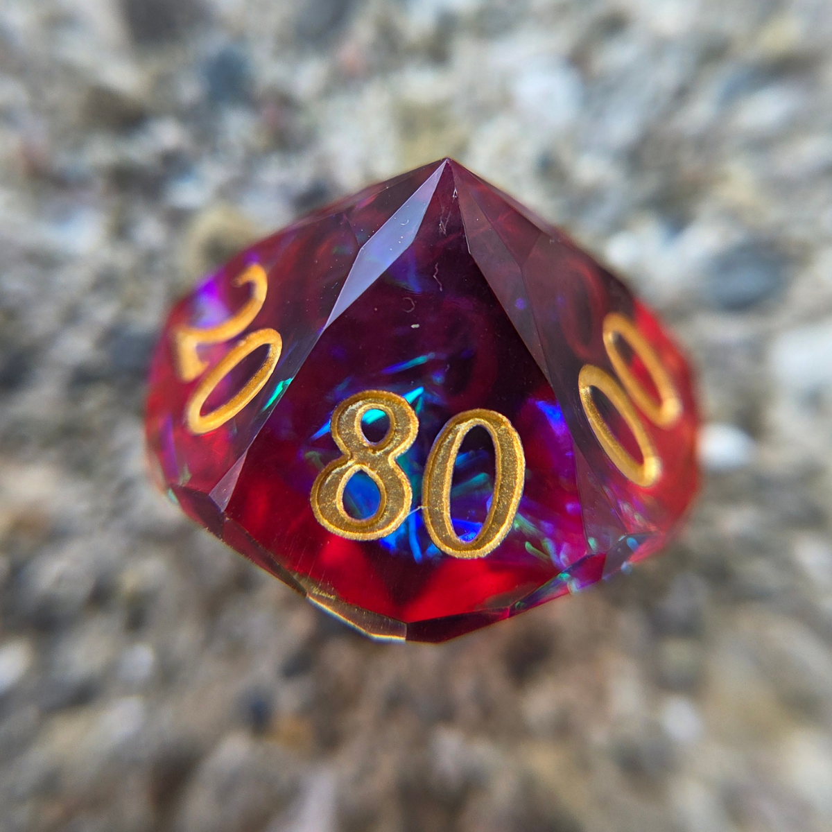 A deep, purplish red die with gold numbers and blue holographic foil