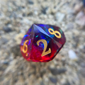 Multicolored die with gold numbers on a blurred natural background