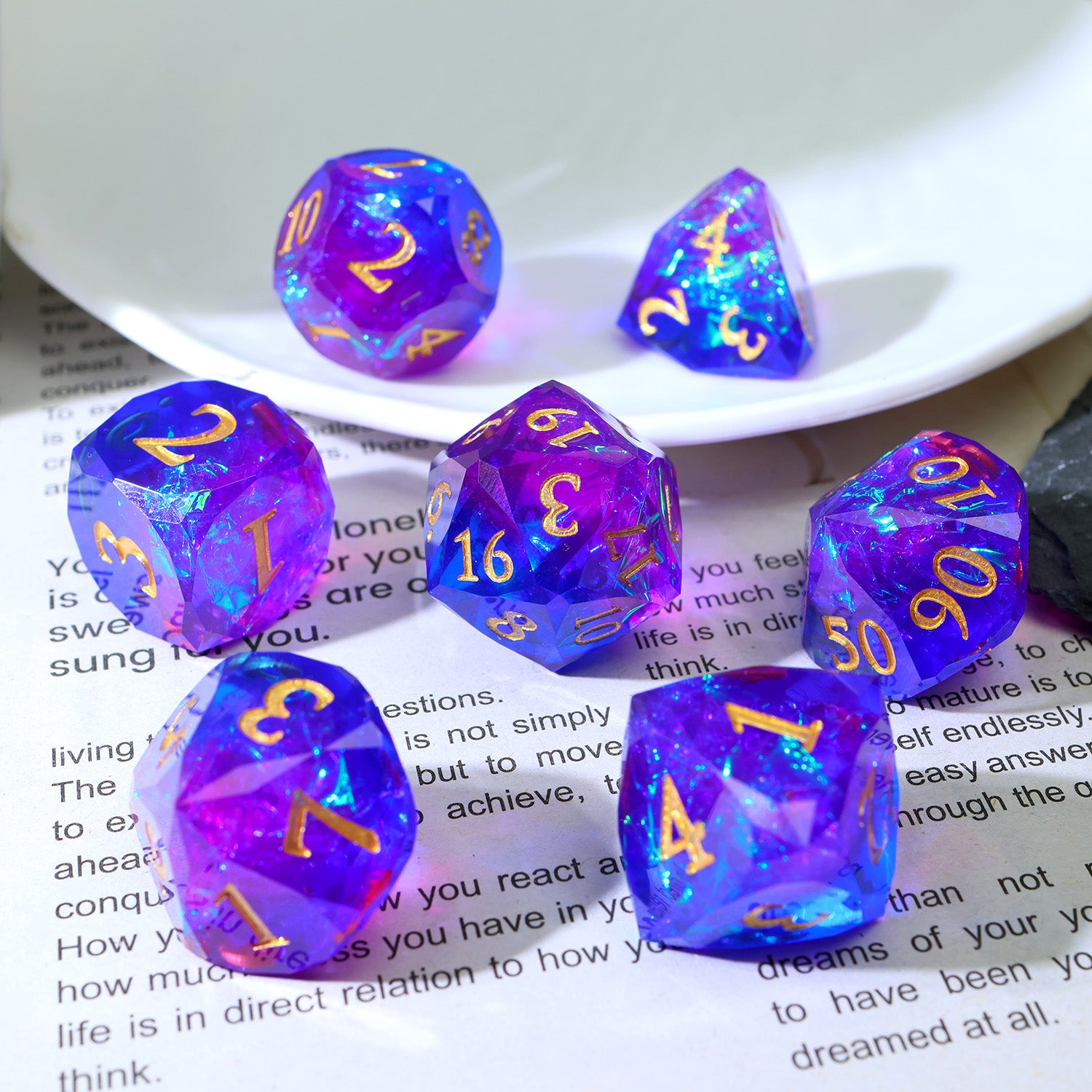Set of purple polyhedral dice with gold numbers sitting on a textbook page and a plate